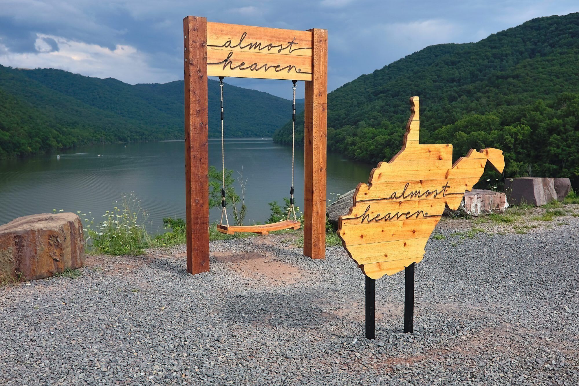 A wooden sign with the text "almost heaven" in a natural setting with a lake and mountains in the background.