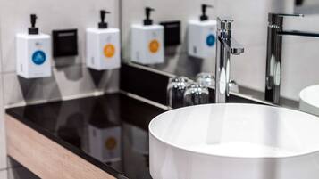 Une salle de bain moderne avec un lavabo rond blanc, un robinet chromé et trois distributeurs de savon de couleurs différentes.