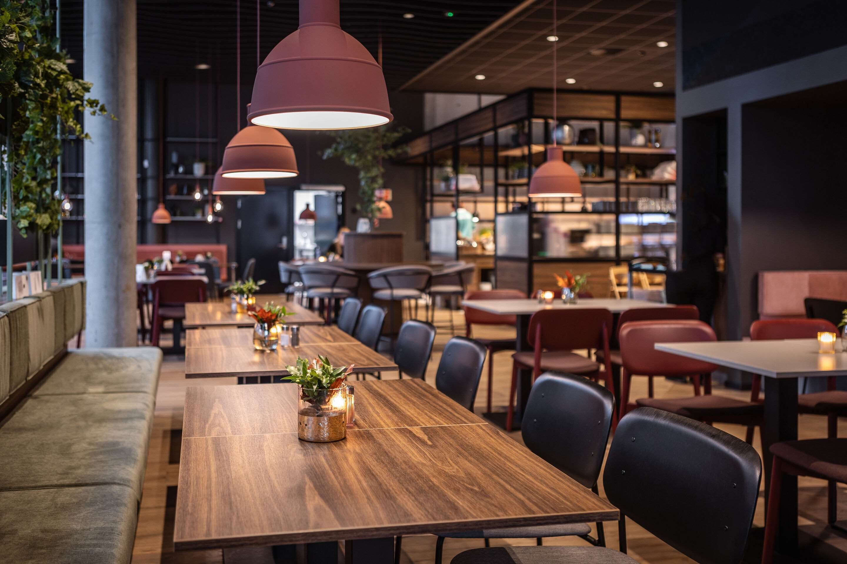 Un ristorante moderno con lunghi tavoli di legno, sedie nere e lampadari a sospensione.