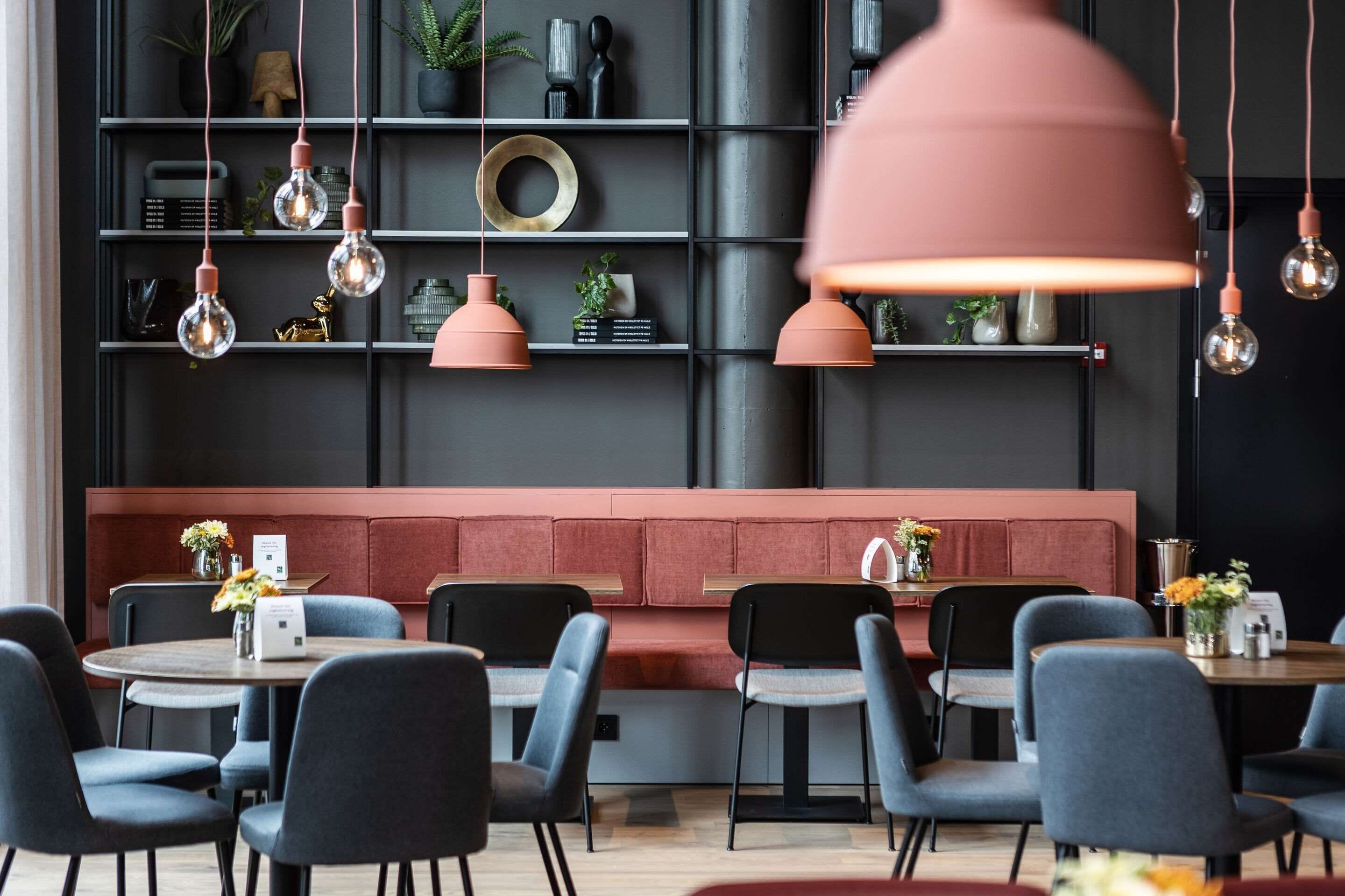 Un restaurante moderno con mesas redondas, sillas negras y un banco con cojín rojo.