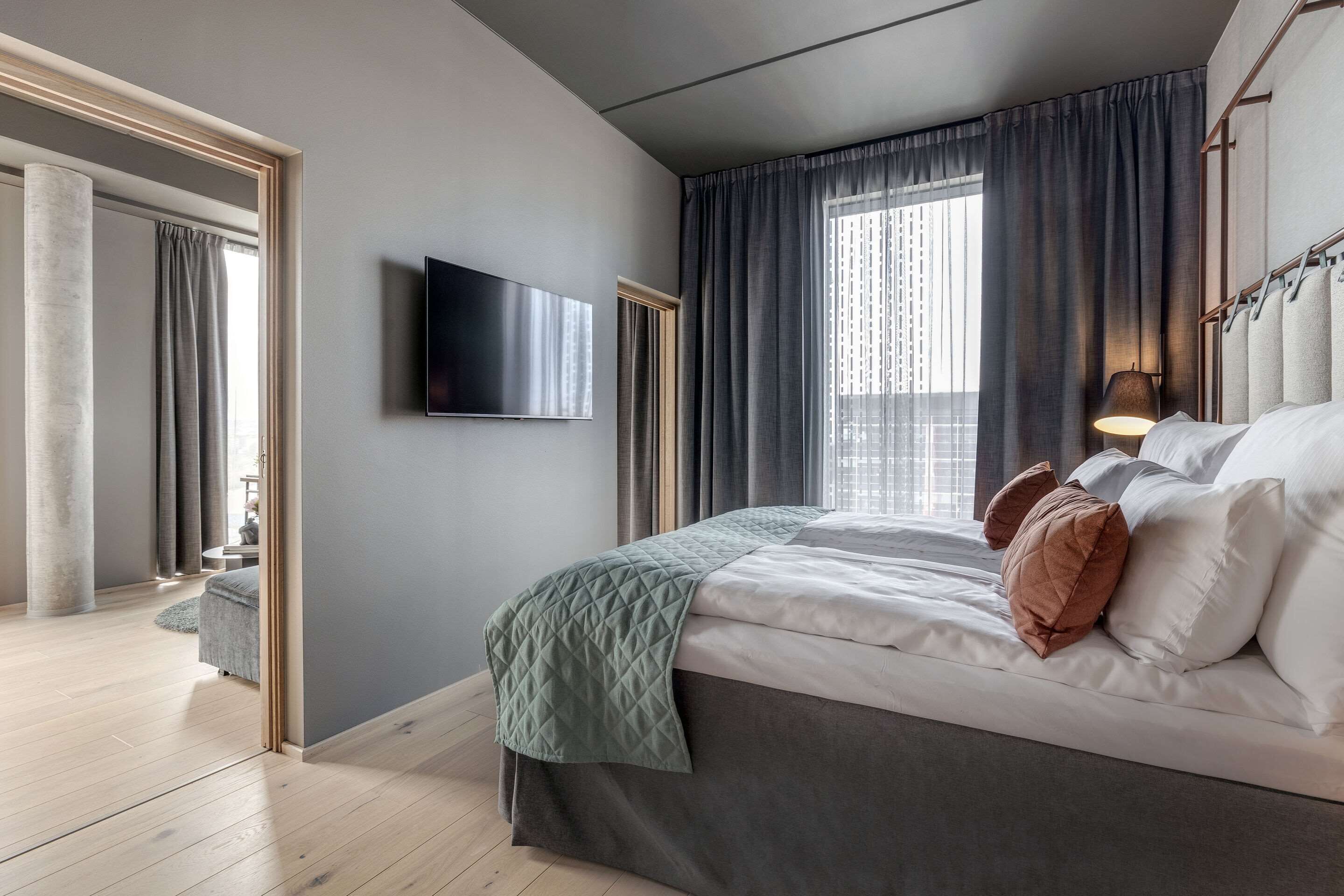 Une chambre d’hôtel moderne avec un grand lit, un téléviseur à écran plat fixé au mur et une vue sur la ville par la fenêtre.