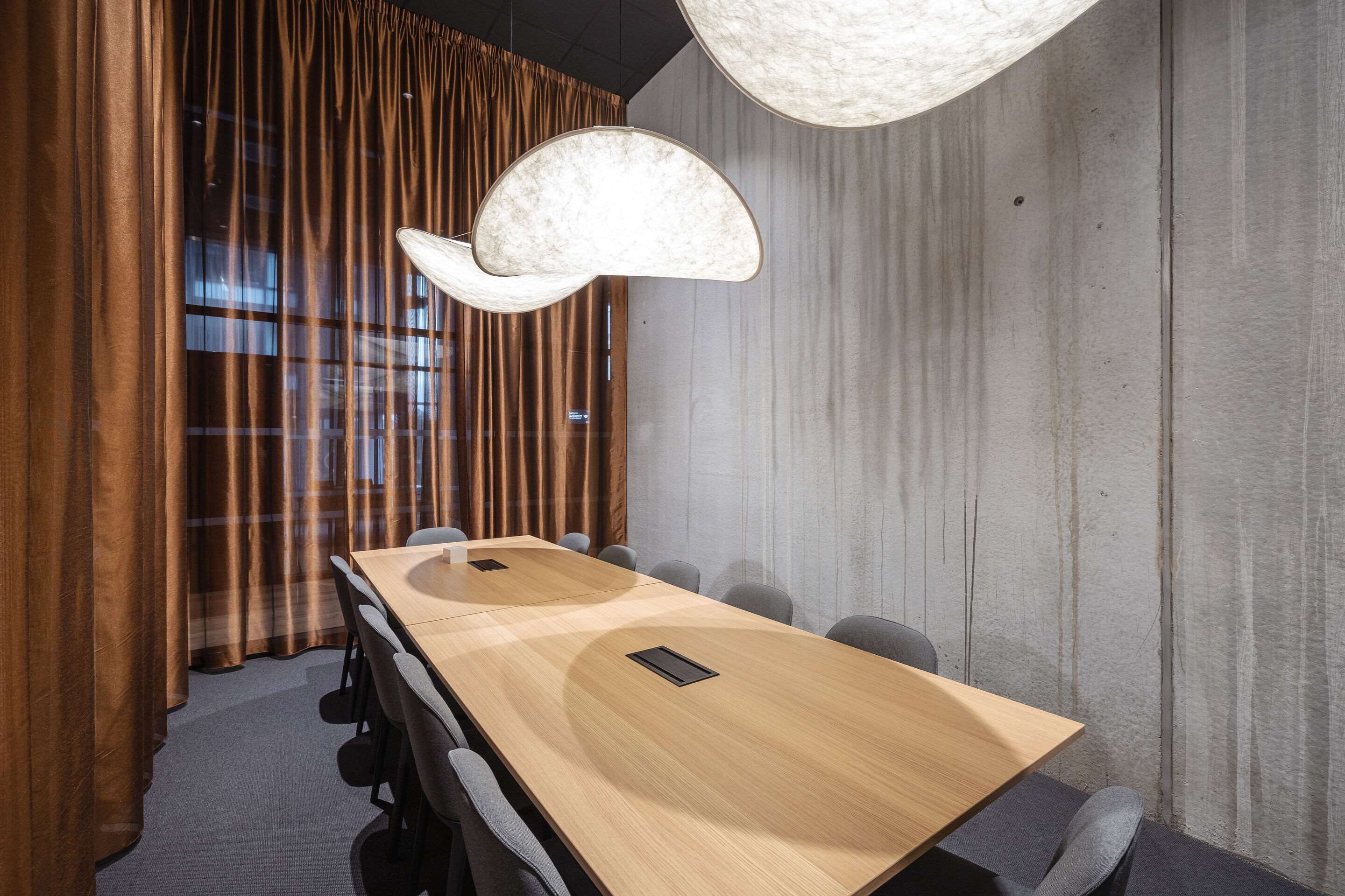 A conference room with a long wooden table, grey chairs, and a unique ceiling light fixture.