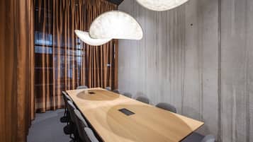 Un salón de conferencias con una larga mesa de madera, sillas grises y una lámpara de techo original.