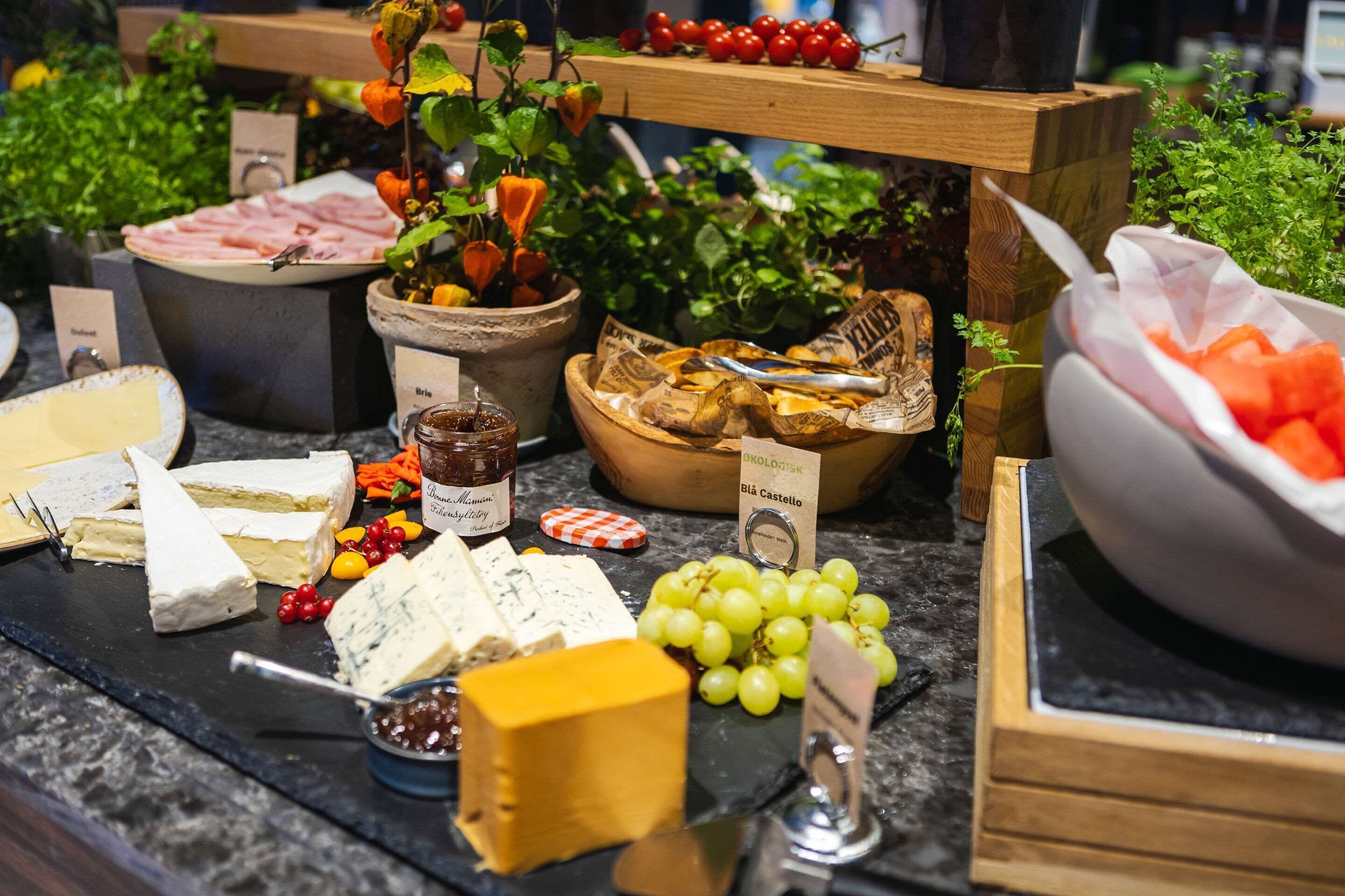 A cheese and charcuterie board with various cheeses, fruits, and a bowl of sliced tomatoes.