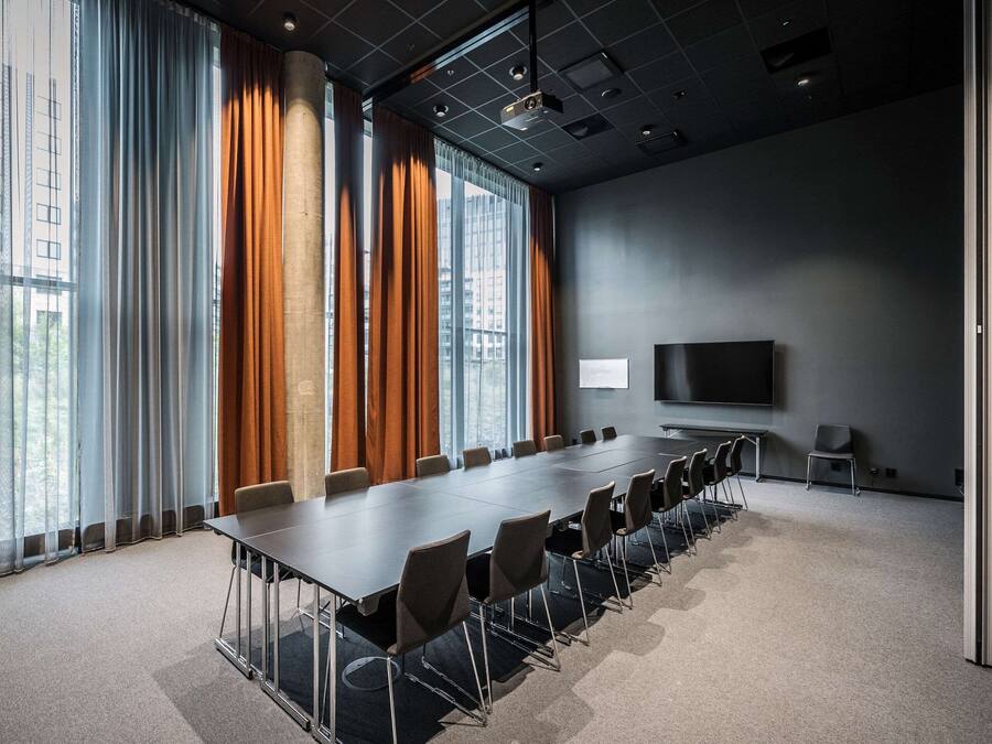 Uma sala de conferências com uma mesa comprida, cadeiras, um projetor e uma tela de televisão.
