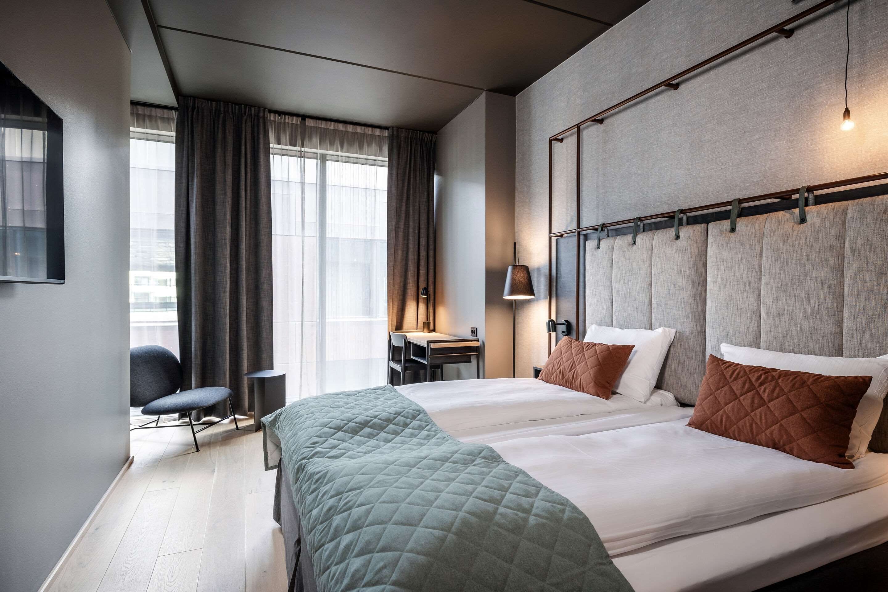 Une chambre d’hôtel avec deux lits, un bureau, une chaise et une grande fenêtre avec des rideaux.