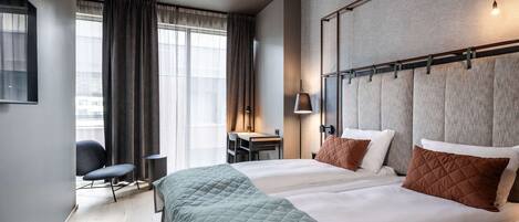 Une chambre d’hôtel avec deux lits, un bureau, une chaise et une grande fenêtre avec des rideaux.