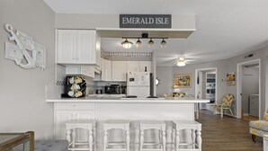 Een keuken met witte kasten, een centraal eiland met krukken, en een bordje met de tekst 'Emerald Isle'.