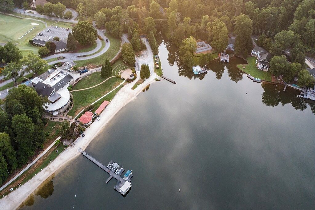 An aerial view of a lakeside property with a dock, a circular building, and surrounding greenery.