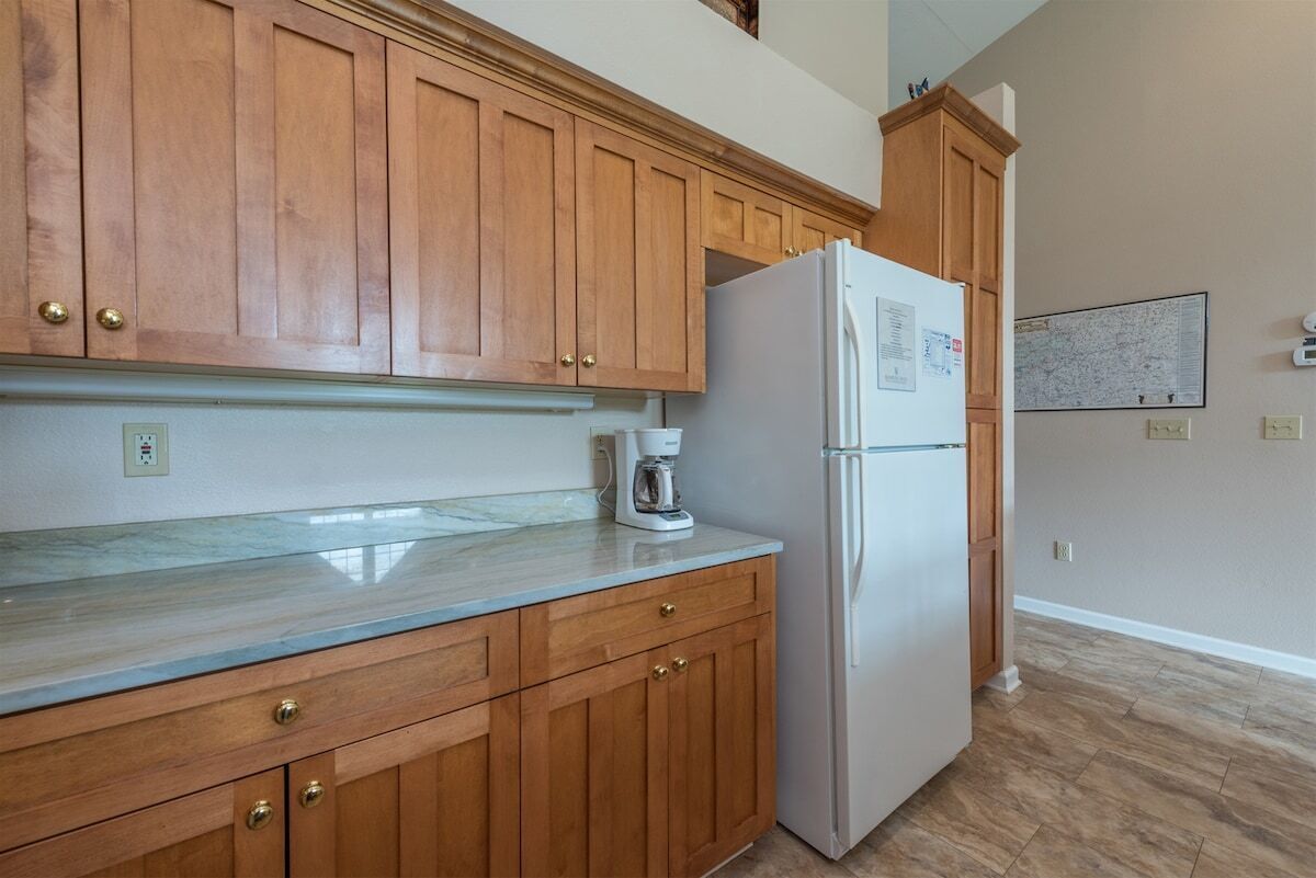 A kitchen with wooden cabinets, a marble countertop, a refrigerator, and a coffee maker.