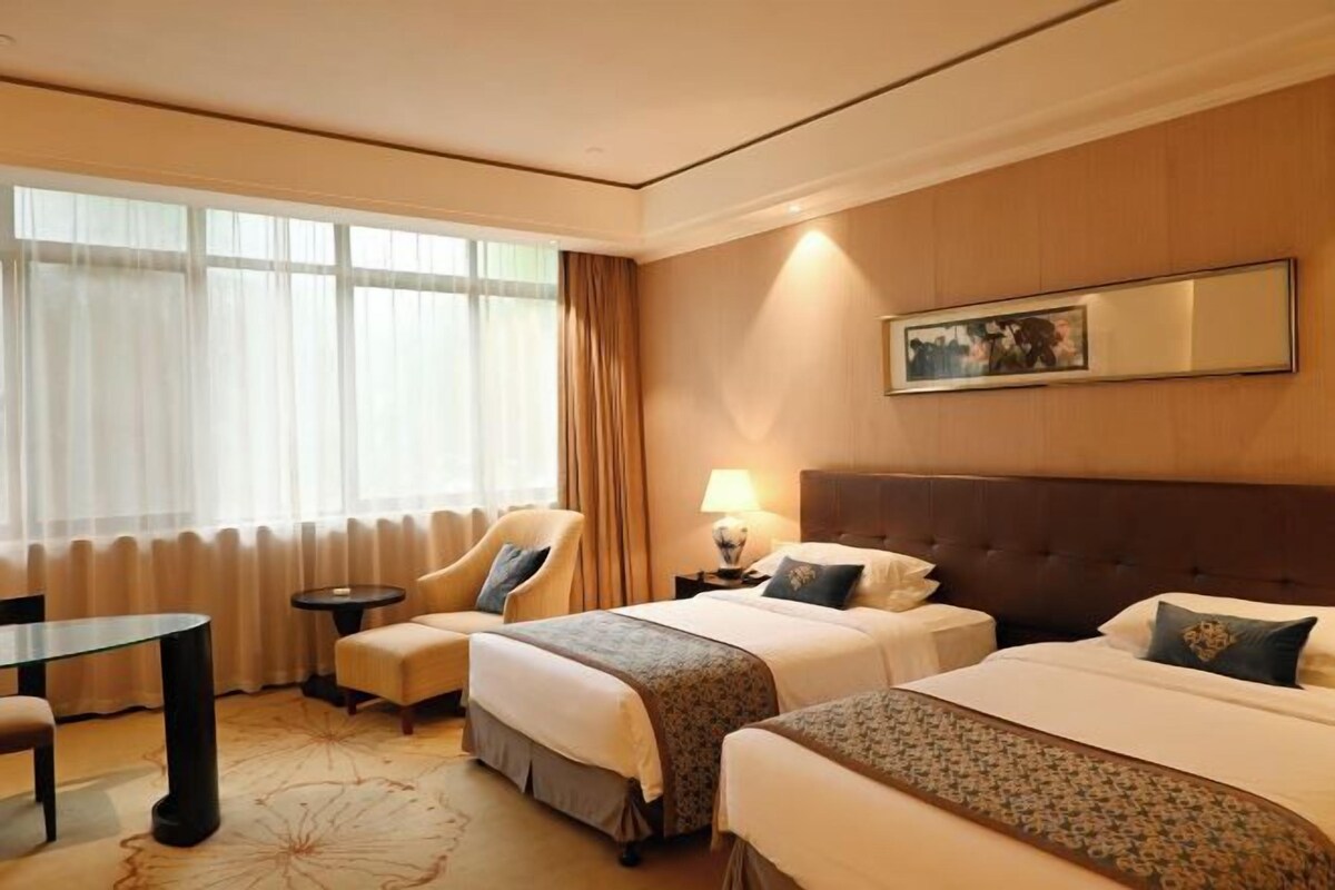 Een hotelkamer met twee bedden, een zithoek, een bureau en een raam met gordijnen.
