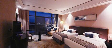 Une chambre d’hôtel avec deux lits, un bureau, une télévision et une vue sur la ville la nuit.