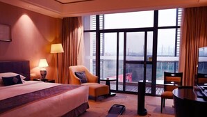 A hotel room with a large bed, a desk, a chair, and a view of the city through large windows. - Jiuhua Chunshenhu Suzhou (Suzhou)