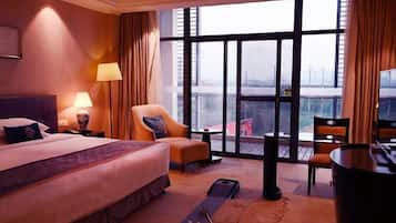 Quarto de hotel com uma cama grande, uma escrivaninha, uma cadeira e vista da cidade através de amplas janelas.