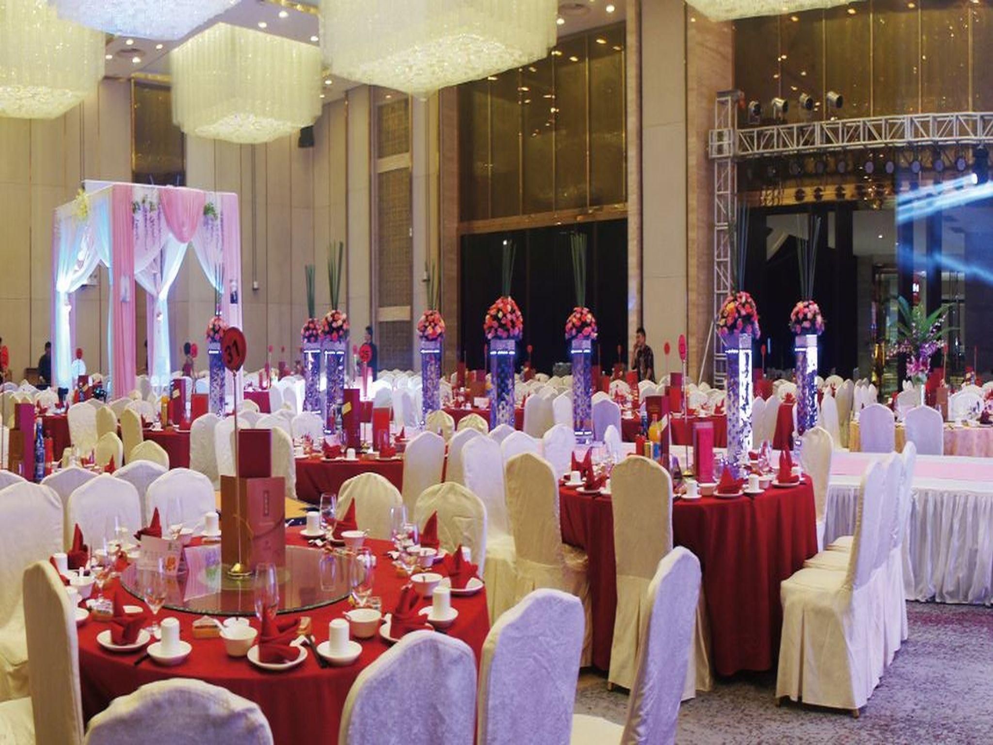 A banquet hall with round tables, white chairs, and red tablecloths.