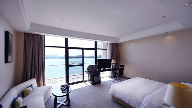 A hotel room with a bed, a desk with a computer, a TV, and a view of the water. - Jiuhua Chunshenhu Suzhou (Suzhou)