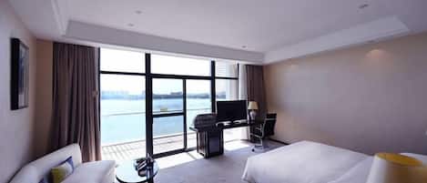A hotel room with a bed, a desk with a computer, a TV, and a view of the water.