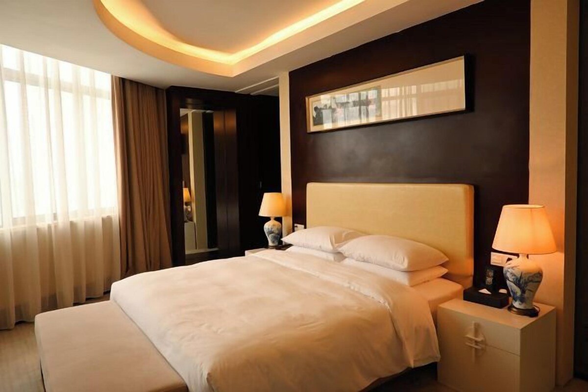 A hotel room with a large bed, bedside lamps, a nightstand, a mirror, and a framed picture on the wall.