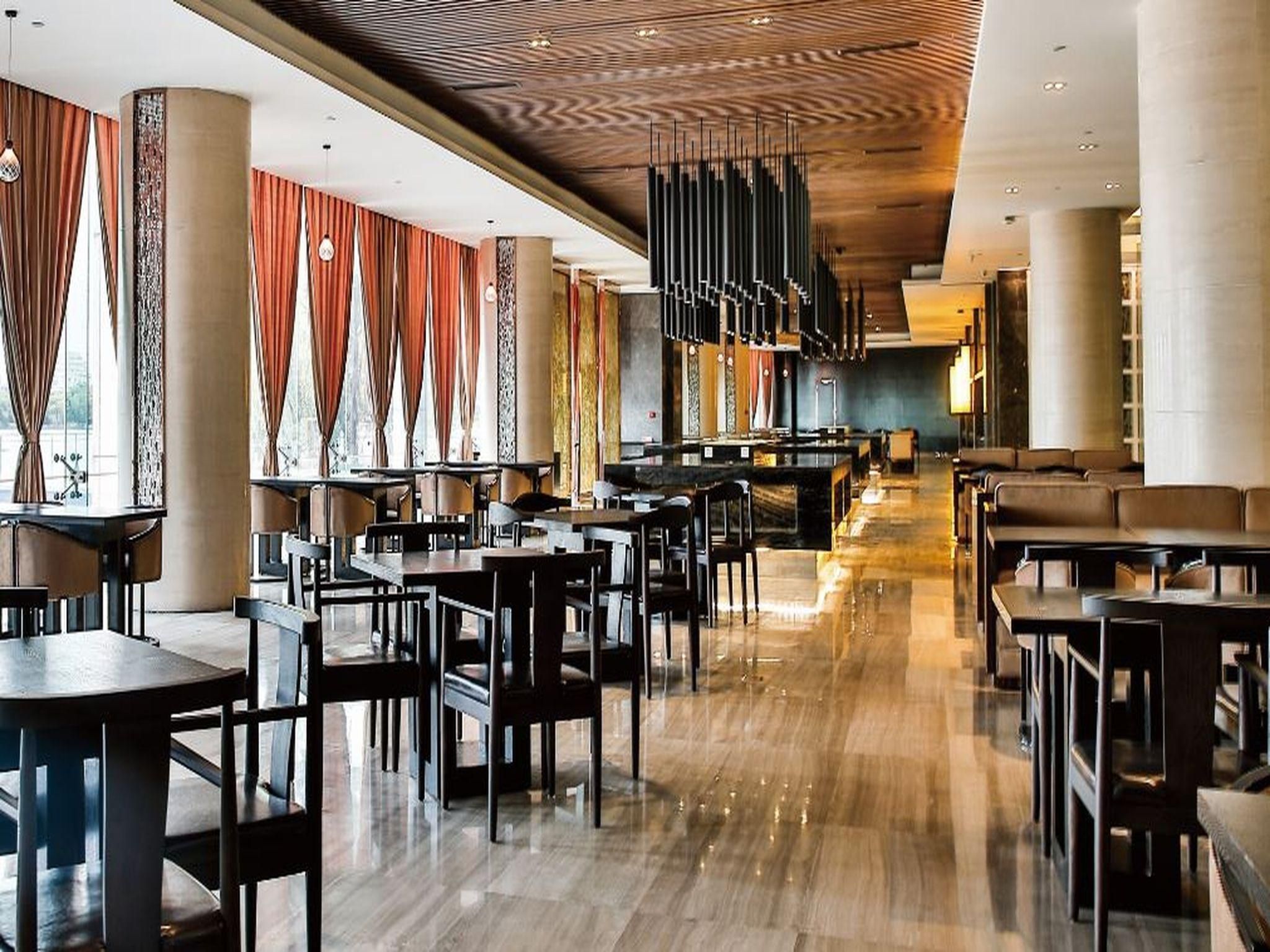 Um restaurante amplo, com pé direito alto, luminárias modernas e diversos tipos de assentos.