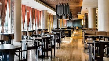Um restaurante amplo, com pé direito alto, luminárias modernas e diversos tipos de assentos.