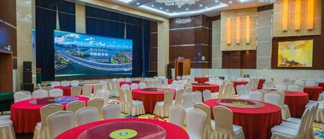 A conference room with multiple round tables, white chairs, and a large screen displaying a presentation.