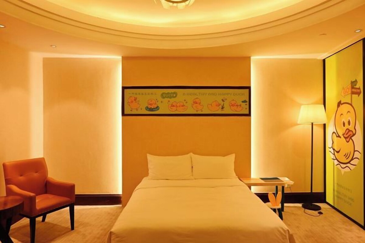Quarto de hotel com cama, cadeira, escrivaninha e parede decorada com personagens de desenho animado.