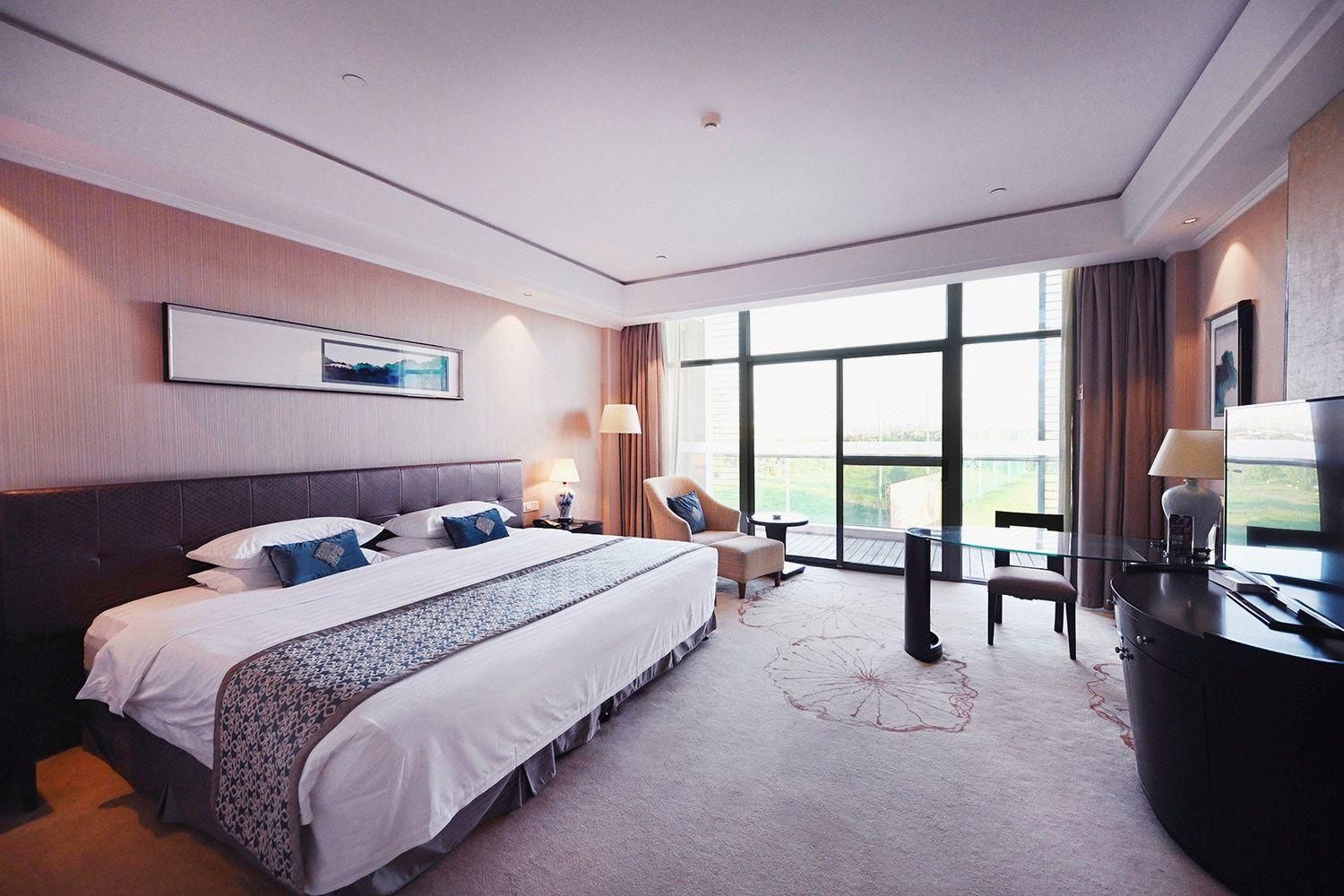 A hotel room with a large bed, a desk, a chair, and a TV.