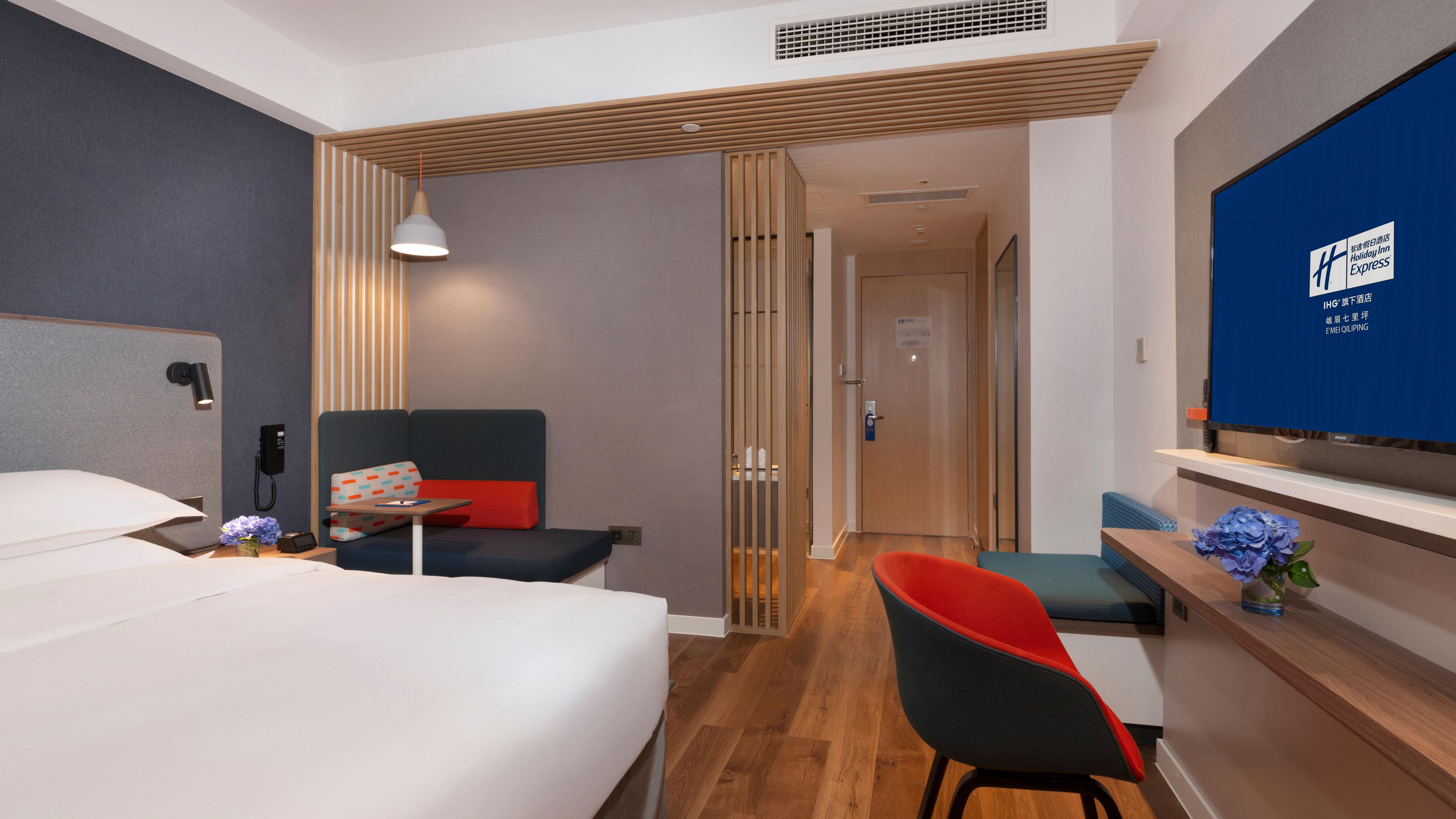 A hotel room with a bed, a desk, a chair, a TV, and a wooden partition.
