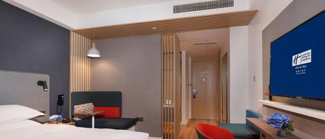 A hotel room with a bed, a desk, a chair, a TV, and a wooden partition.