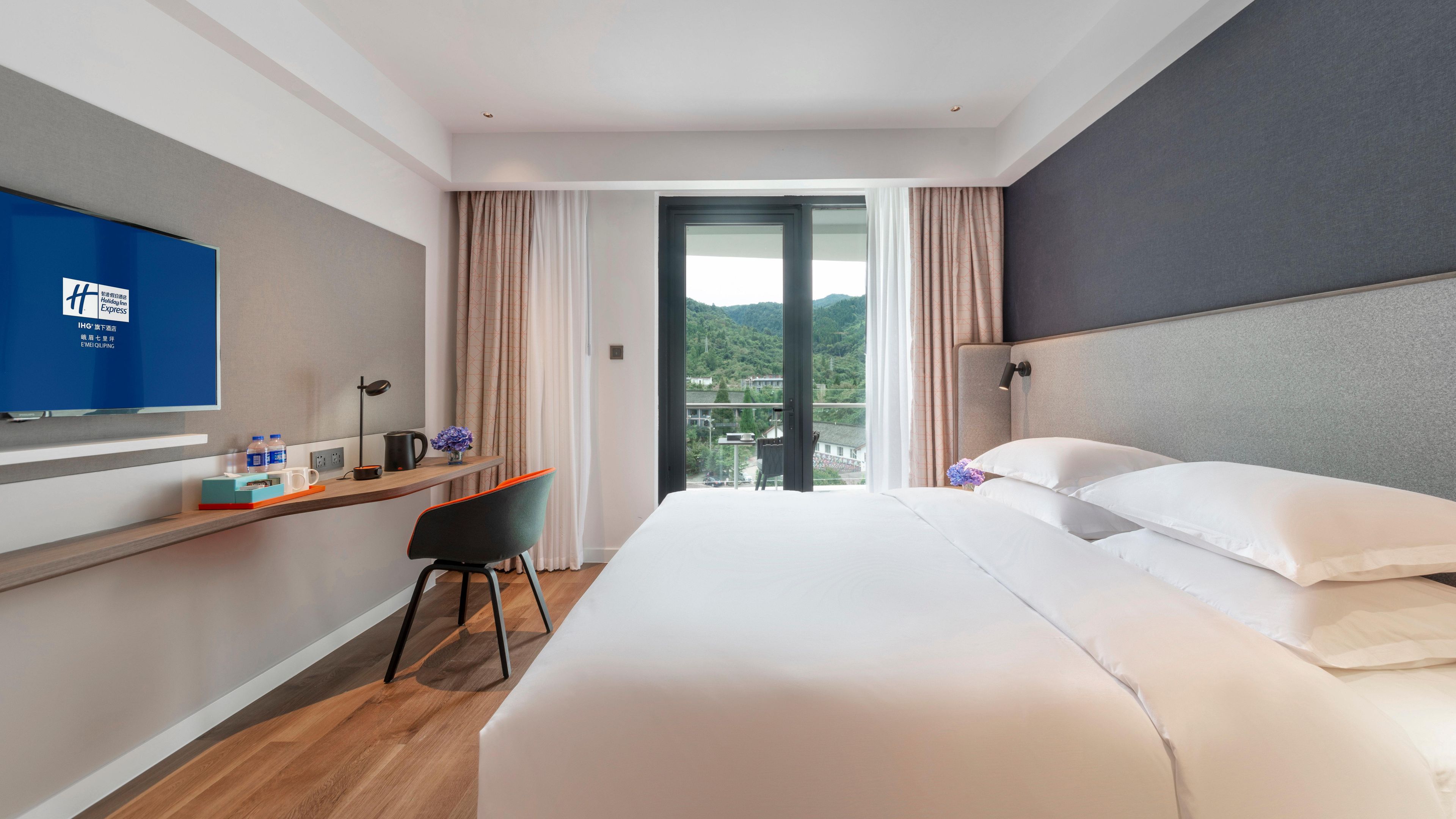 Camera d'albergo con un letto, una scrivania con una sedia, una televisione e vista su un paesaggio montuoso.