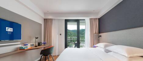 Habitación de hotel con una cama, un escritorio con silla, televisión y vistas a un paisaje montañoso.