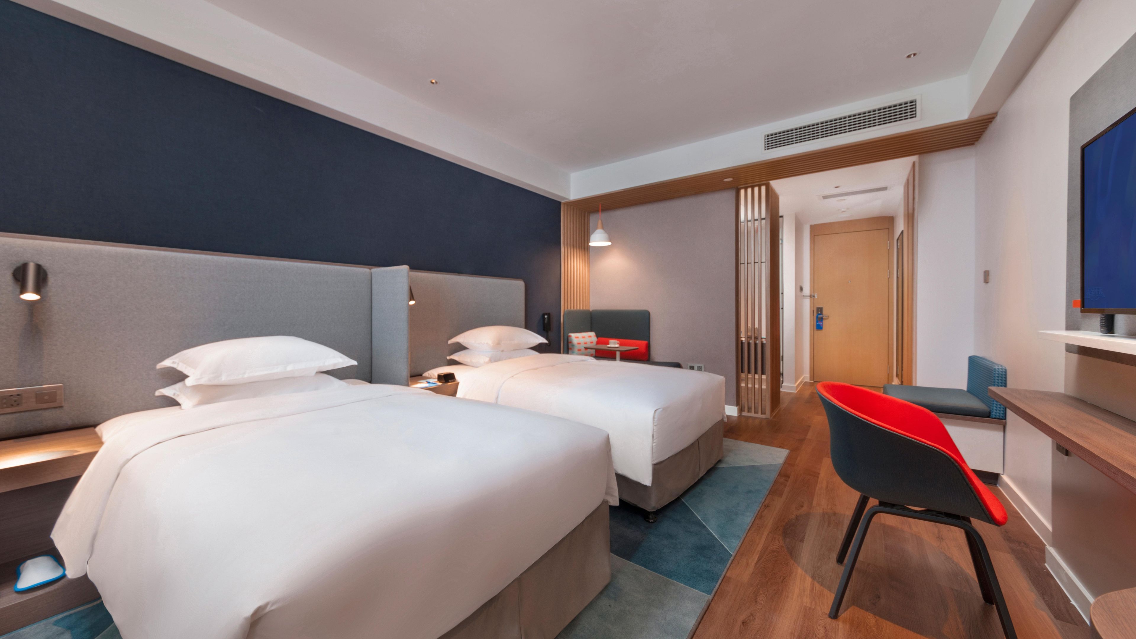 A hotel room with two beds, a desk, a chair, a TV, and a bathroom door.