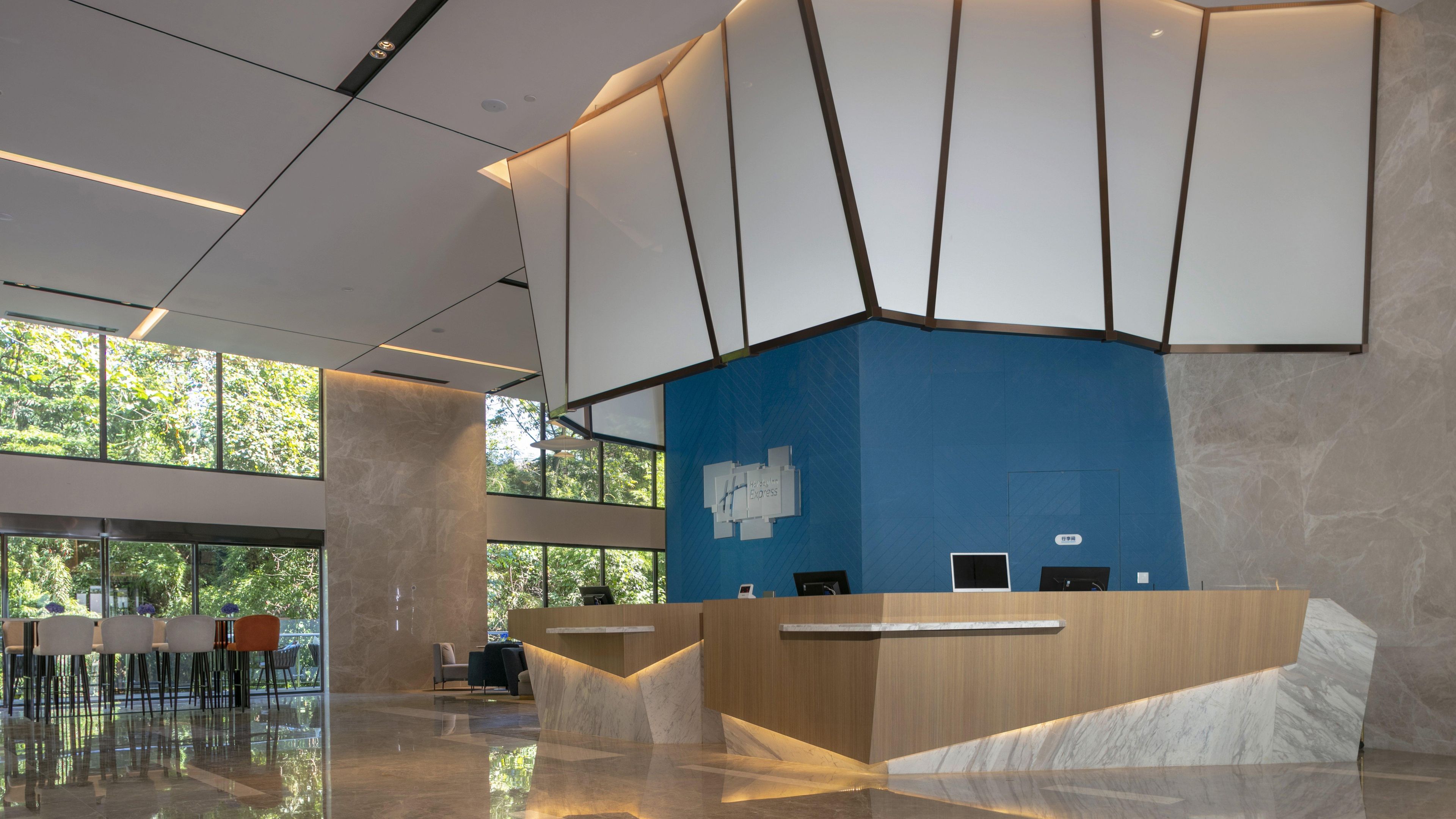 A modern reception desk with a blue accent wall, a glass partition, and a seating area with chairs and tables.