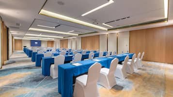 Un salón de conferencias con filas de mesas, sillas blancas y manteles azules.