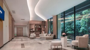 Een moderne hotellobby met een gebogen plafond, een zithoek, een bijzettafeltje en een groot raam met uitzicht op een bos.