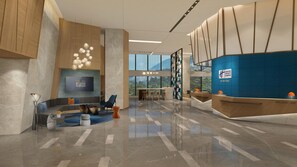 Een moderne hotel lobby met een receptiebalie, zithoek en een groot televisiescherm.