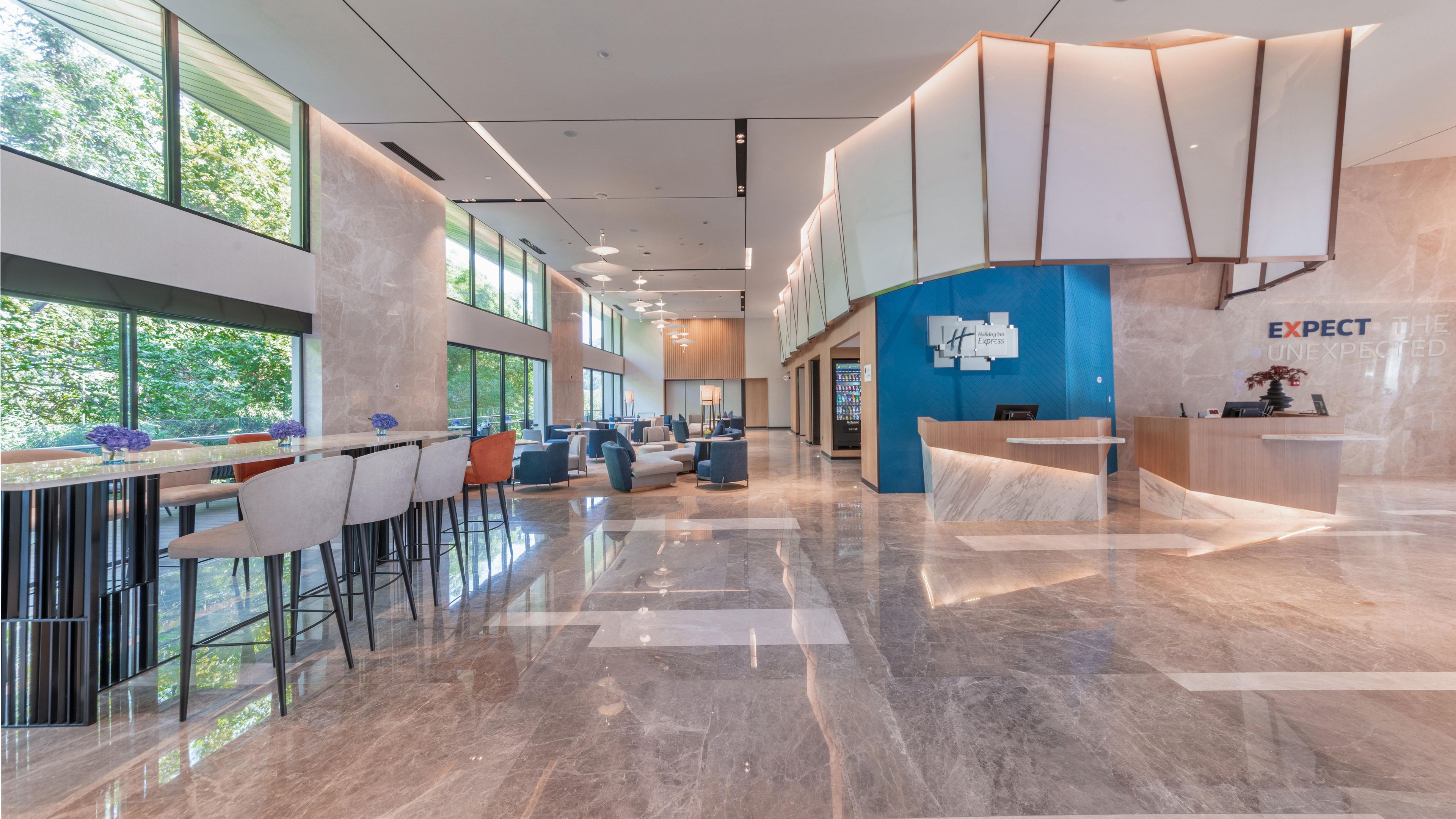A modern hotel lobby with a reception desk, seating area, and large windows offering views of the outdoors.