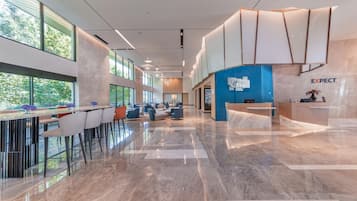 A modern hotel lobby with a reception desk, seating area, and large windows offering views of the outdoors.