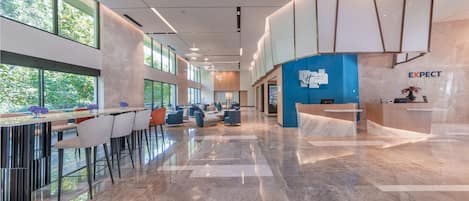 Un moderno vestíbulo de hotel con mostrador de recepción, zona de estar y amplios ventanales con vistas al exterior.