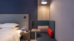 Een hotelkamer met een bed, nachtkastje, telefoon en een klein tafeltje met een stoel.