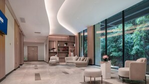 A modern hotel lobby with a curved ceiling, a sofa set, a coffee table, and a large window with a forest view. - Holiday Inn Express E'mei Qiliping (Leshan)