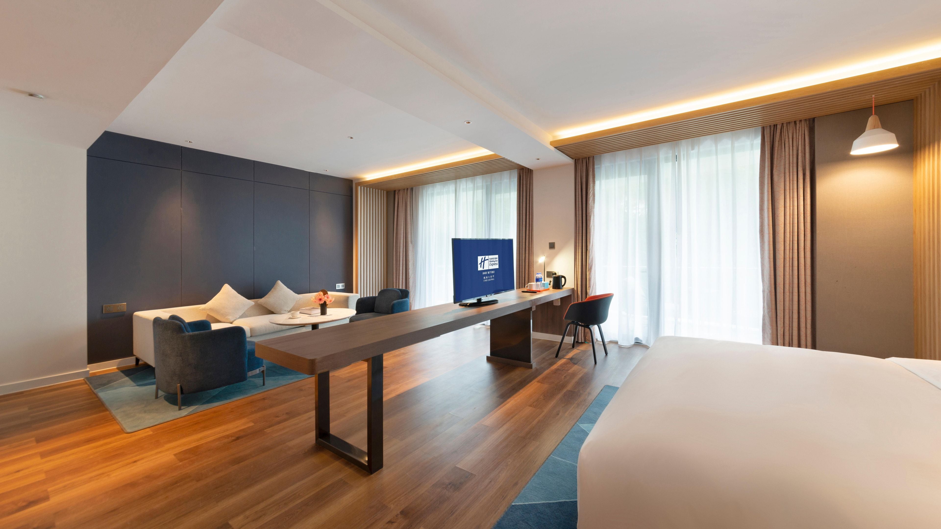 Una habitación de hotel moderna con cama, sofá, escritorio y ventanas amplias.