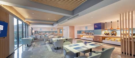 A modern hotel dining area with a long counter, multiple tables, and chairs.