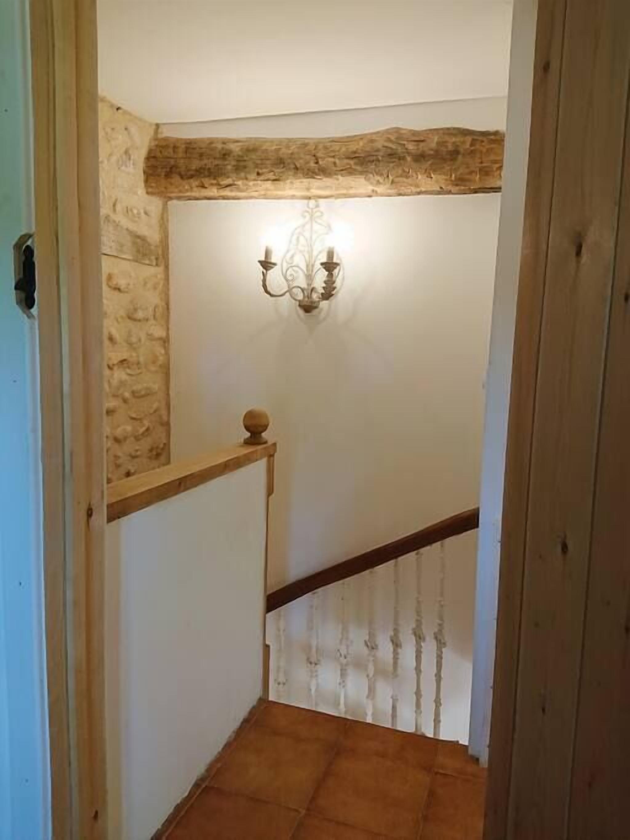 Eine schmale Treppe mit einem hölzernen Geländer und einer dekorativen Wandleuchte.