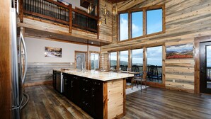 A spacious kitchen with a large island, wooden floors, and large windows offering views of the outdoors.