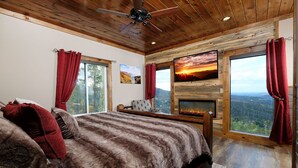 A bedroom with a large bed, a fireplace, and a scenic view through the windows.