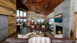 A spacious living room with a stone fireplace, leather sofas, and a large TV.
