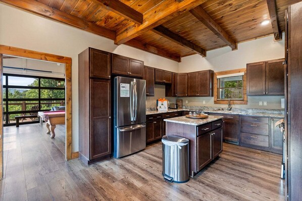 A modern kitchen with wooden cabinets, a stainless steel refrigerator, and a large island with a sink. - Moonlit Lodge - Hot Tub, Modern Vibes & Firepit (Sevierville)