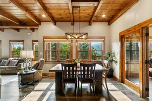 A dining area with a wooden table and chairs, large windows with a view of greenery, and a ceiling with wooden beams. - Moonlit Lodge - Hot Tub, Modern Vibes & Firepit (Sevierville)