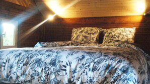 Een kamer met een houten plafond, een bed met bloemenprint beddengoed en twee wandlampen.